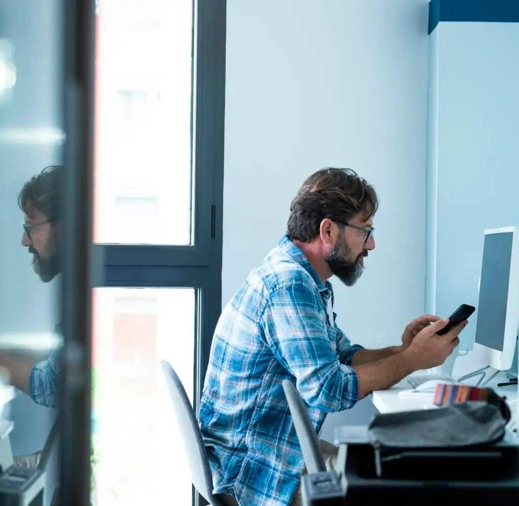 Adult business man work at office with mobile phone and desktop computer. Job and technology