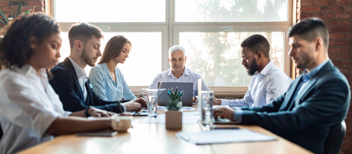Colleagues Working During Corporate Meeting Sitting At Desk In Office