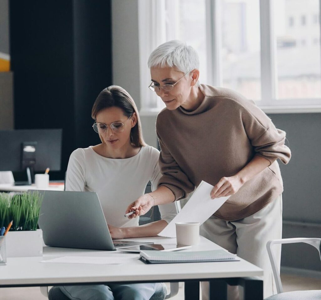 Two confident businesswomen looking at computer monitor while working in the office together